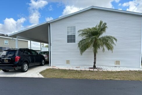 White mobile home with a palm tree and carport under a blue sky.