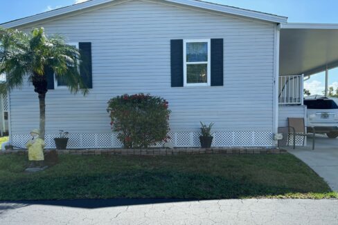 White brick house exterior with a window and plants in front.